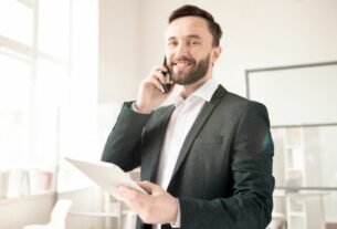 Corretor de seguros atendendo cliente ao telefone enquanto analisa documentos, representando o trabalho de orientação e consultoria em seguros.