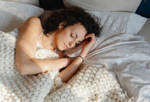Mulher dormindo de lado em cama iluminada pela luz natural, representando rotina de descanso adequada, qualidade do sono e bem-estar físico e mental.