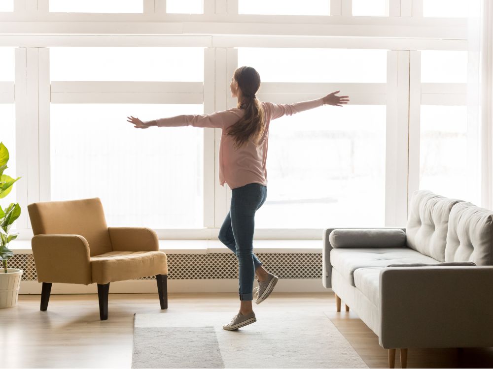 Pessoa em apartamento iluminado comemorando a conquista de morar sozinho, representando planejamento de mudança e dúvidas comuns como o que é uma kitnet ao escolher um imóvel para viver.