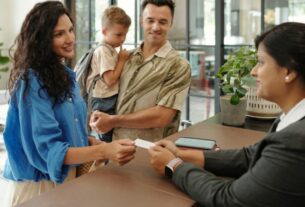Família sendo atendida na recepção de empresa, realizando cadastro com a recepcionista em balcão de atendimento organizado.