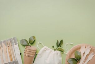 Itens reutilizáveis e ecológicos organizados sobre fundo verde, incluindo copos de papel, talheres de madeira e bolsa sustentável, representando práticas de sustentabilidade nas empresas e uso de sacola de tnt.