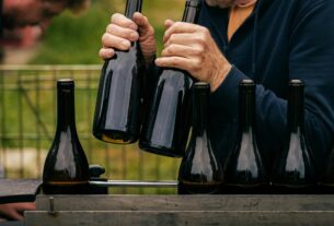 Pessoa manuseando garrafas de vinho durante o processo de envase artesanal, organizando as garrafas sobre bancada ao ar livre.