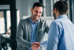 Dois profissionais apertando as mãos em ambiente corporativo, demonstrando confiança, parceria e fechamento de acordo de negócios.